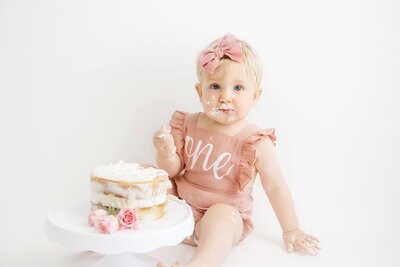 Houston Family Photographer - picture of baby girl turning one with her white birthday cake with pink flowers.