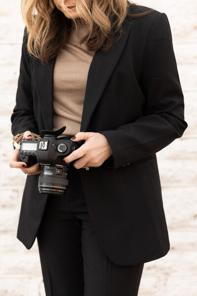 woman standing in a white wall looking at the back of a camera
