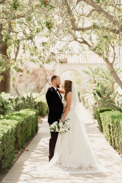 bride and groom facing eachother standing in a walkway under a canopy of trees with beautiful backlight at spanish hills club in camarillo, ca taken by magnolia west photography