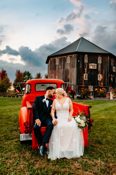 ohio wedding couple look at each other sitting on red vintage truck in front of wedding venue