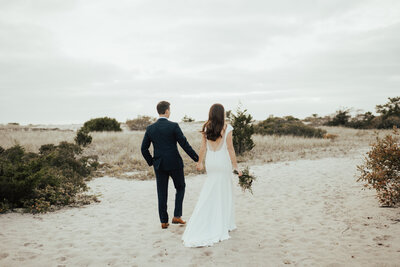bride and groom holing hands walking on beach