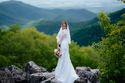 bride standing on rocks while holding her bridal bouquet with mountains in the background