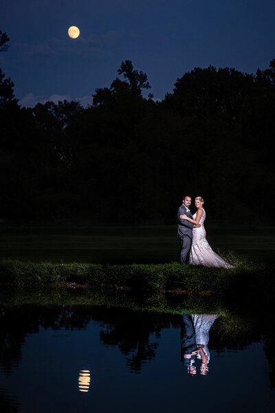 a bride and groom pose for their wedding photographer in Austin under a full moon by a lake