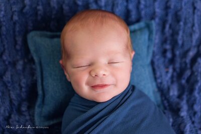 A smiling baby boy wrapped in a soft blue blanket, radiating joy and innocence.
