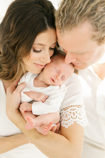 mom and dad holding newborn baby in white