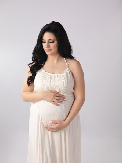 pregnant mother holding belly in white boho dress for studio portraits
