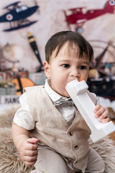 Smiling girl wearing a glittering red princess dress and silver tiara, seated on the grass with hands resting on her cheeks in a sunny outdoor setting.