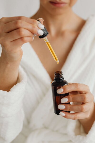 Ayurvedic Skin Specialist, Jen, wearing a white top and pants sitting on a jute rug leaning against a neutral couch