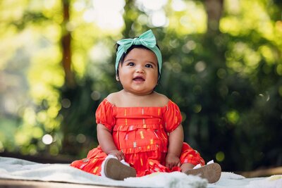 A cheerful baby girl wearing an orange dress sits on a cozy blanket, radiating joy and innocence.