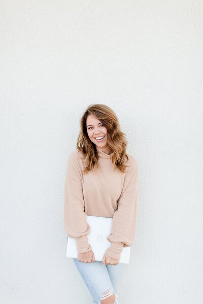 Woman standing against a white wall holding a laptop