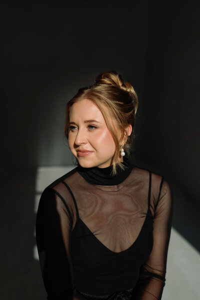 Elegant portrait of photographer Kelly Lugo wearing sheer black bodysuit with dramatic shadows in the background