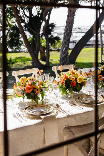 orange roses and yellow flower centerpieces with mixed metal place settings from window perspective