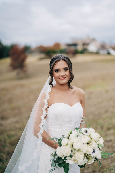 woman in white dress with veil holding a bouquet of flowers smiling at the camera