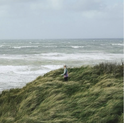 Einzelne Person steht in einer Düne und schaut auf das Meer.