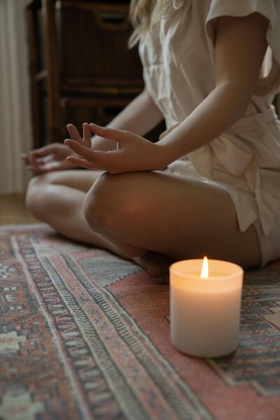 Blonde woman sitting on rug sits in meditation in candlelight