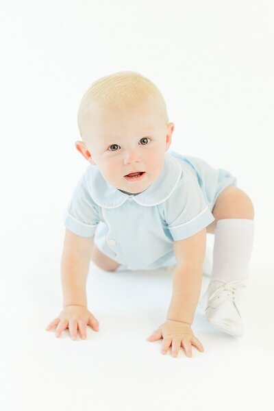studio milestone of one year old little boy crawling white backdrop