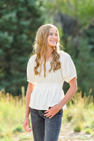 A high school senior girl stands in the sunlight in a grassy field at Tibble Fork Reservoir in American fork in the spring