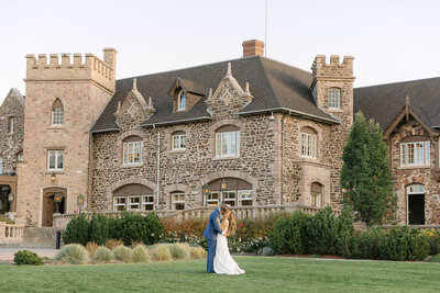 Bride and groom standing in front of historic stone highlands ranch mansion with manicured lawn – fine art Colorado wedding prints