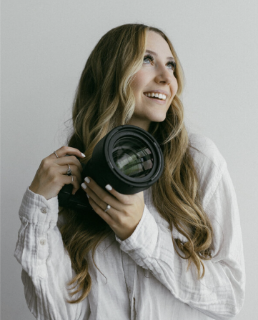 A photo of Brooke holding a camera smiling to the right of the camera.