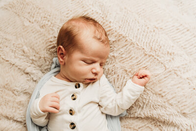 A little newborn baby boy snuggles into a soft blanket for a lifestyle newborn photoshoot at the studio