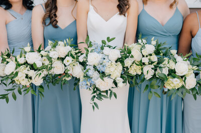 Bride and bridesmaids hold white bouquets while wearing blue and white dresses at this Ackerhurst Dairy Farm wedding in Bennington, NE. Photo by Anna Brace, who specializes in Omaha Wedding photography