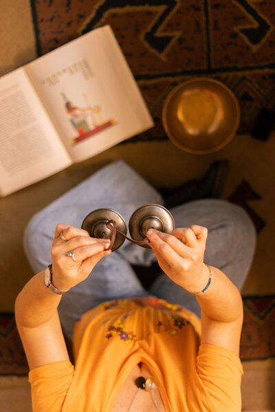 Prise de vue en plongée, on voit Leslie assise en tailleur dans une librairie. Elle tient une paire de Tingsha (2 petites cymbales reliées entre elles par un lacet de cuir, instrument du Tibet). Devant elle sont posés un libre ouvert et un bol chantant en métal.  