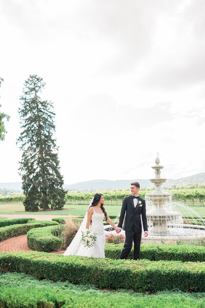 A newlywed couple walking around a small fountain in a garden