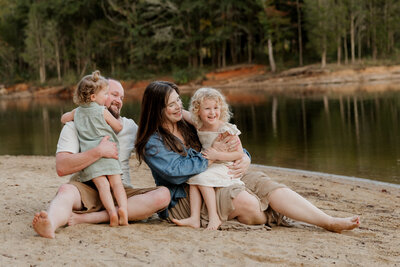Family laughing and playing together in grassy Raleigh park during outdoor portrait session, photographed by Moments by Hiba.