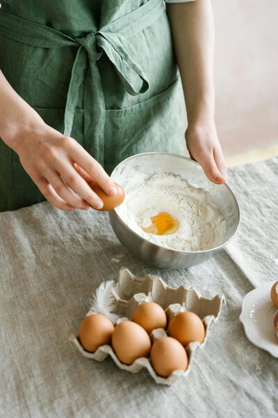A woman’s hands arranging fresh eggs and herbs in a kitchen, representing community, nourishment, and joyful preparation for new life.