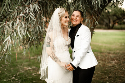 Wedding portraits of lgbtq couple standing and smiling under tree in Tucson, Arizona