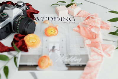 Wedding magazine surrounded by a Canon camera, red cloth, and flowers