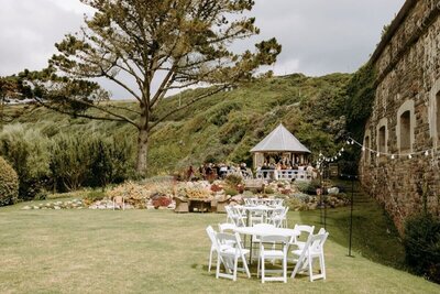 A lawn with white tables and chairs with bunting around and a summerhouse in the background