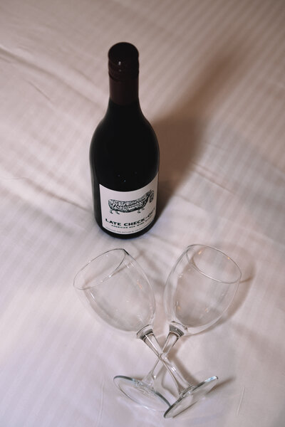 Wine bottle and two glasses on Hampton Roads luxury inn bed with white linens - hospitality photography