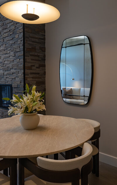 Close-up of a travertine dining table with white boucle chairs and wood accents styled in the luxury dining room of a Park City Airbnb, designed by Sister Studio.