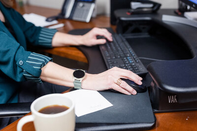 Bethany typing on a keyboard next to a cut of coffee