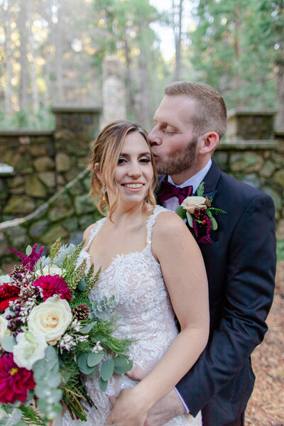 groom kisses bride in a snowy forest