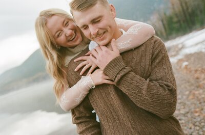 couple hugging and laughing on the shore of lake mcdonald