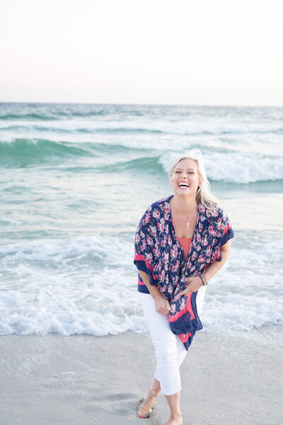 woman laughing towards camera with ocean behind her