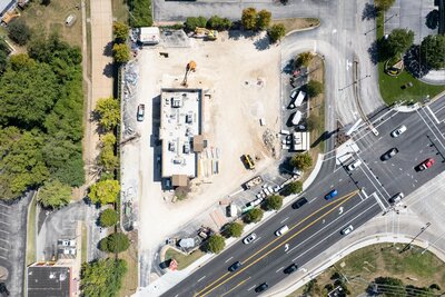 Drone photograph of a construction site showing a building being worked on, cleared land around it, and equipment.