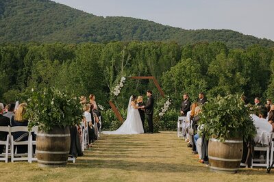 Wedding ceremony in North GA at Yonah Mountain Vineyard holding hands exchanging vows as all the guest look on