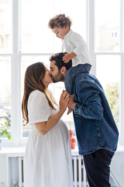 Pregnant couple kissing  with little boy on father's shoulders at a maternity photo shoot in Kensington