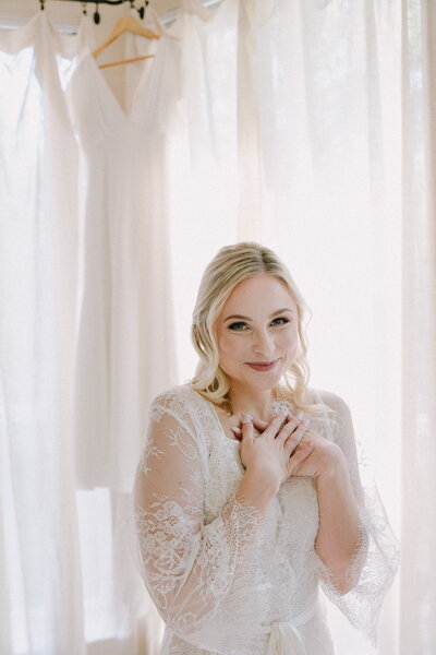Bride smiles in lace robe while getting ready for her wedding day.
