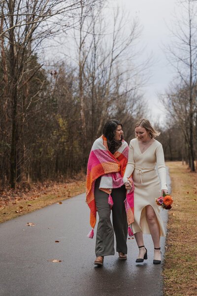 Two women walk down a street with a blanket around them