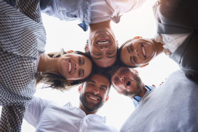 Five smiling adults looking down in a circle, heads close together.
