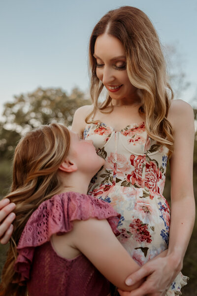 Mom in floral dress hugs and smiles at her daughter while playing with her hair during family pictures at Kansas City Family Photoshoot.