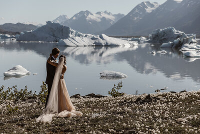 Bride and groom sanding on a shore of a iceberg filled lake in Alaska