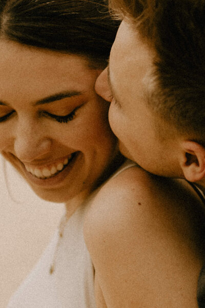 Close-up image of a boy kissing his fiancé on the cheek while she laughs