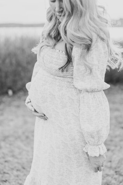 Expecting mother with long hair holds belly and dress in maternity photoshoot