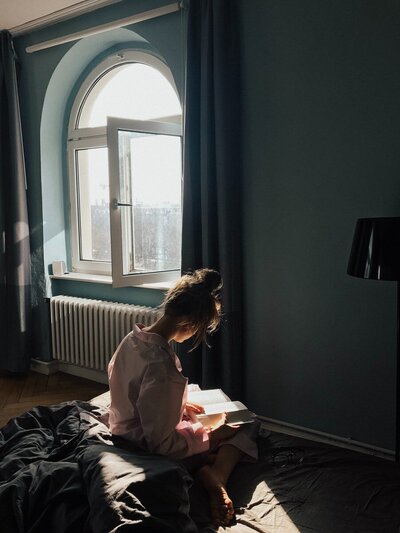 woman reading a book in front of a window with sunlight streaming in