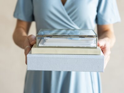 Close-up of a woman in a blue dress holding a stack of heirloom photo albums and keepsake boxes from a Kansas City photography studio.